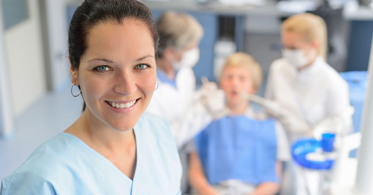 Two dentists performing a procedure on a patient with a third dental professional in view.